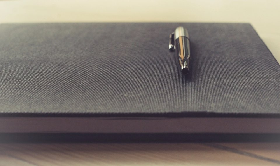 Caderno escuro com caneta sobre a mesa, pronto para anotar a pauta