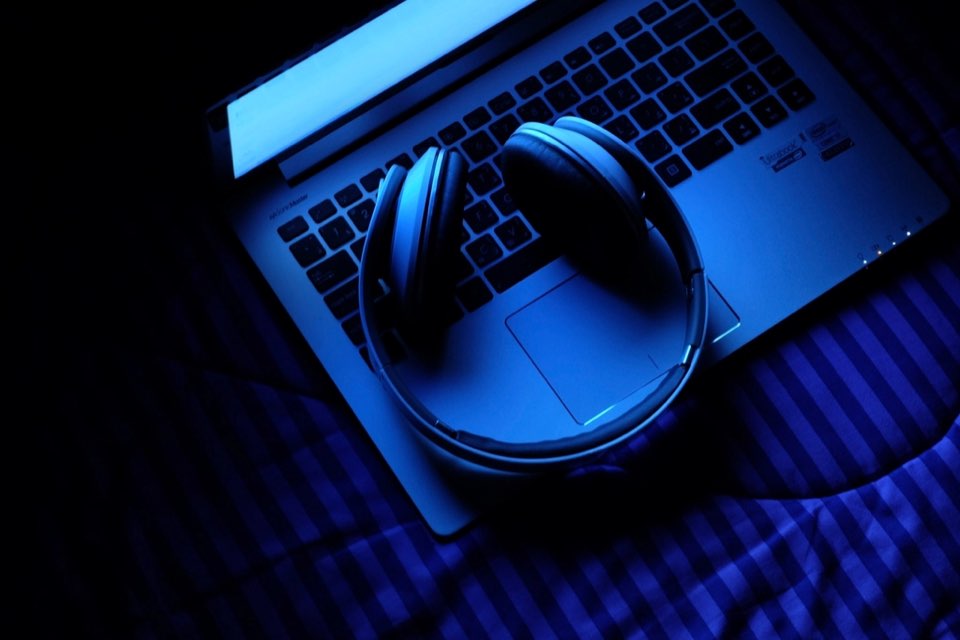 Fones de ouvido sobre teclado de laptop em ambiente escuro e azulado