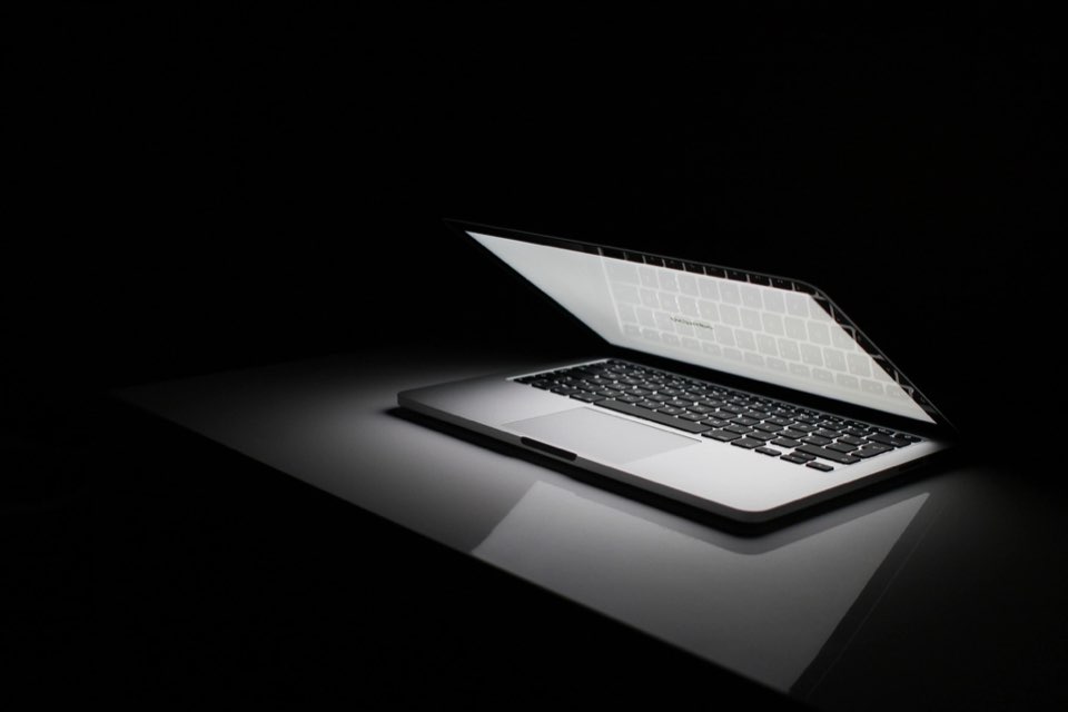 Laptop aberto no escuro com tela iluminada sobre fundo preto